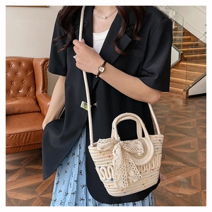 Close-up of a woven straw bucket bag with lace bow decoration and a single pearl accent