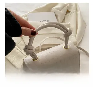 Macro shot of cream mini handbag showing crocodile texture and knotted round handle