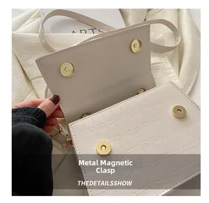 Detail shot of beige faux crocodile leather bag featuring a gold magnetic snap closure