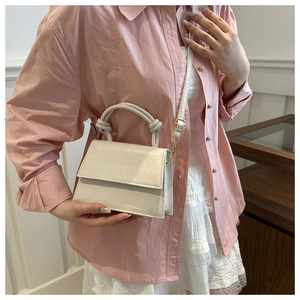 Detail of beige crocodile embossed small square bag with knot handle on shoulder