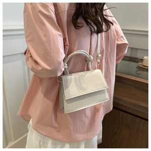 Detail of white crocodile pattern crossbody bag with unique knot handle and gold hardware