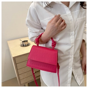 Close-up of vibrant pink faux leather handbag with crocodile pattern and knotted handle