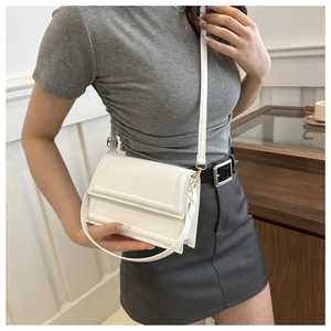 Detail of white leather crossbody bag with minimalist flap design and gold hardware