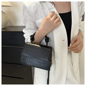 Close-up of black faux crocodile texture handbag with unique knotted handle design