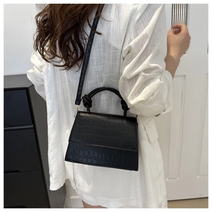 Detail of a black faux crocodile skin crossbody bag with a unique knotted top handle