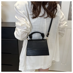Detail of black crocodile pattern crossbody bag with knot handle and gold hardware