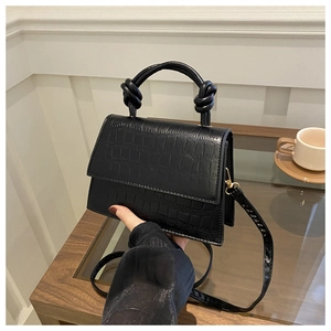Detail of black crocodile texture handbag with unique knot handle and gold hardware