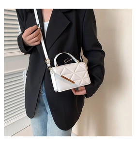 Close-up of white quilted crossbody bag with gold metal trim and paperclip handle detail