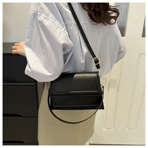 Minimalist black matte leather crossbody bag with golden buckle shown on a model
