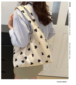 Sac fourre-tout en toile beige avec imprimés cœurs noirs porté à l'épaule par un mannequin