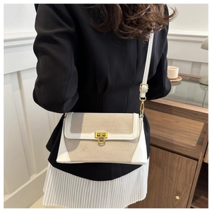 Detail of a white leather and beige canvas crossbody bag with elegant gold metal clasp