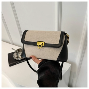 Detailed view of beige canvas crossbody bag with black leather trim and golden metal clasp
