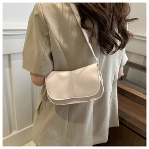 Dettaglio di una borsa a tracolla minimalista beige in pelle indossata con cuciture raffinate