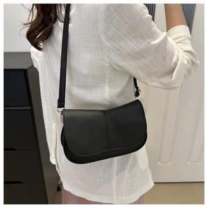 Borsa a sella minimalista in pelle nera con patta e fibbie d'oro su modella