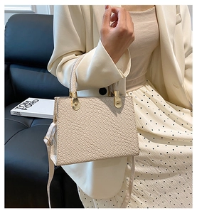 Detail of beige faux leather handbag with snake pattern embossing and gold hardware detail