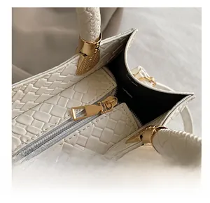 Close-up of smooth gold metal zipper and woven texture on white patent leather handbag