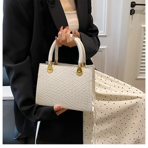 Detail of white woven texture handbag with gold hardware styled with a black suit