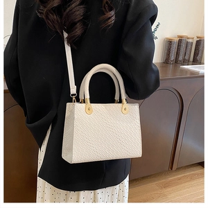 Close-up of white crocodile pattern handbag with gold metal hardware and slim strap