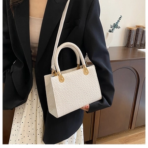 Detailed view of white crocodile pattern handbag with gold hardware and top handles