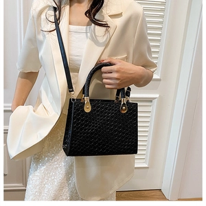 Detail of black woven texture leather handbag with gold hardware held by a model