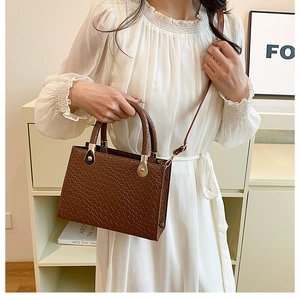Close-up of brown woven textured handbag with round handles on a cream bookshelf