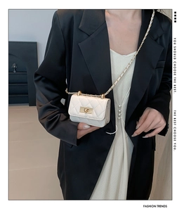 Close-up of white quilted mini bag with gold twist lock and chain strap on model
