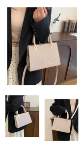 Detail of beige crocodile pattern handbag with gold hardware and top handle shown on a desk