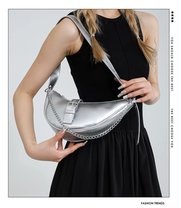 Detail of silver crescent moon shoulder bag with decorative chains and wide strap