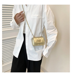 Close-up of golden quilted mini bag with chain strap worn by a model in a white shirt