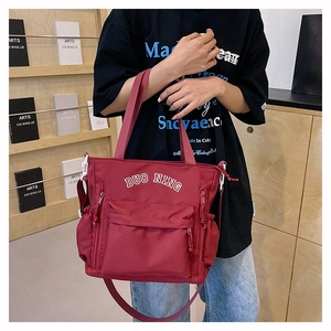 Detail of red large capacity nylon tote bag with multi-zipper pockets and white lettering