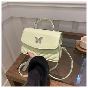 Détail d'un sac à main matelassé vert clair avec fermoir papillon argenté sur table en bois