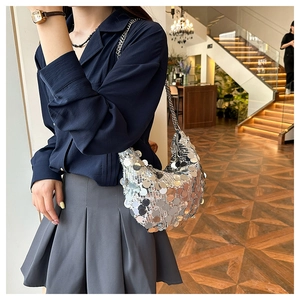 Dettaglio di borsa hobo con paillettes argento e tracolla a catena indossata da modella