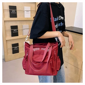 Detail of burgundy nylon crossbody bag featuring multiple zippers and adjustable strap