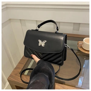 Détail d'un sac bandoulière matelassé noir avec boucle papillon argentée et coutures en V