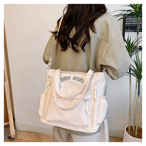 Detail view of large cream tote bag featuring side drawstrings and front zipper pockets