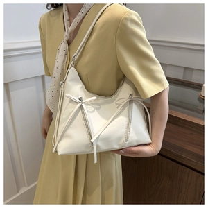 Detail of soft cream shoulder bag with bow ribbons and zipper decor on a dress