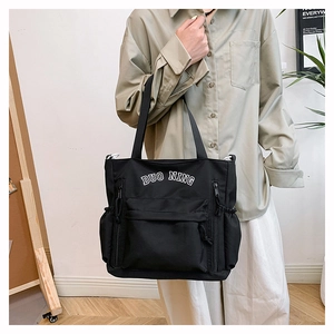 Detail of black large-capacity nylon tote bag with white lettering and side pockets