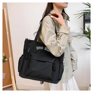 Model wearing a black canvas tote bag with DUO NIA print in a modern home setting