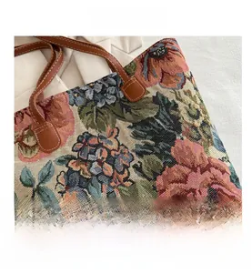 Detailed close-up of floral tapestry fabric with brown faux leather handle and white stitching