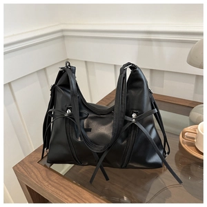 Detail of black matte tote bag featuring bow ribbons and dual vertical zippers on wood surface