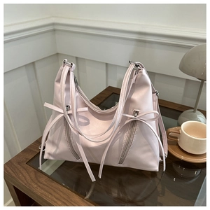 Detail of light pink bucket bag with ribbon bows and zippers on a wooden table