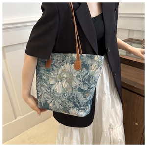 Close-up of vintage blue floral jacquard tote bag with brown leather handles worn by model