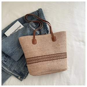 Detail of woven straw tote bag with brown embroidery and leather handles on linen