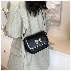 Detail of a black quilted crossbody bag featuring a silver metal bow and chain strap