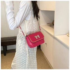 Detail of rose red crossbody bag with silver bow accent and quilted leather texture