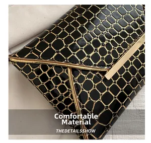 Detail von schwarzem Krokodil-Strukturstoff mit goldener Metallschiene auf Umschlagtasche