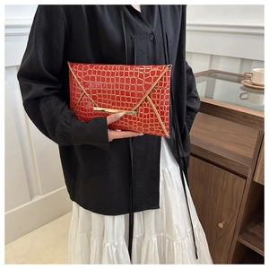Detail der roten Briefumschlag-Clutch mit Krokoprägung und elegantem Goldrand