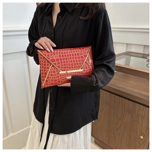 Detail of red crocodile texture envelope clutch bag with gold metallic V-shaped trim