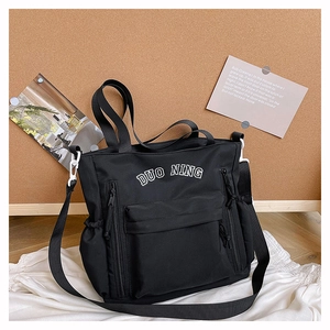 Close-up of black canvas tote bag with white letter embroidery and drawstring side pockets