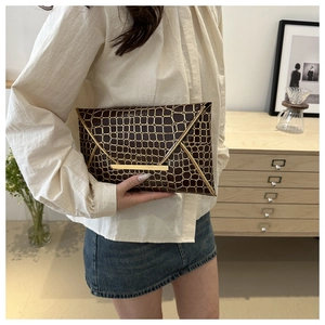 Detail der dunkelbraunen Clutch in Kroko-Optik mit goldenem Gittermuster und Metallbesatz